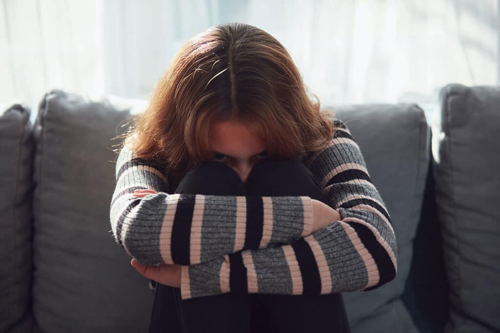 Ung kvinde sidder krøbet sammen på en sofa med armene om knæene, et udtryk for angst og overbelastning ved autisme