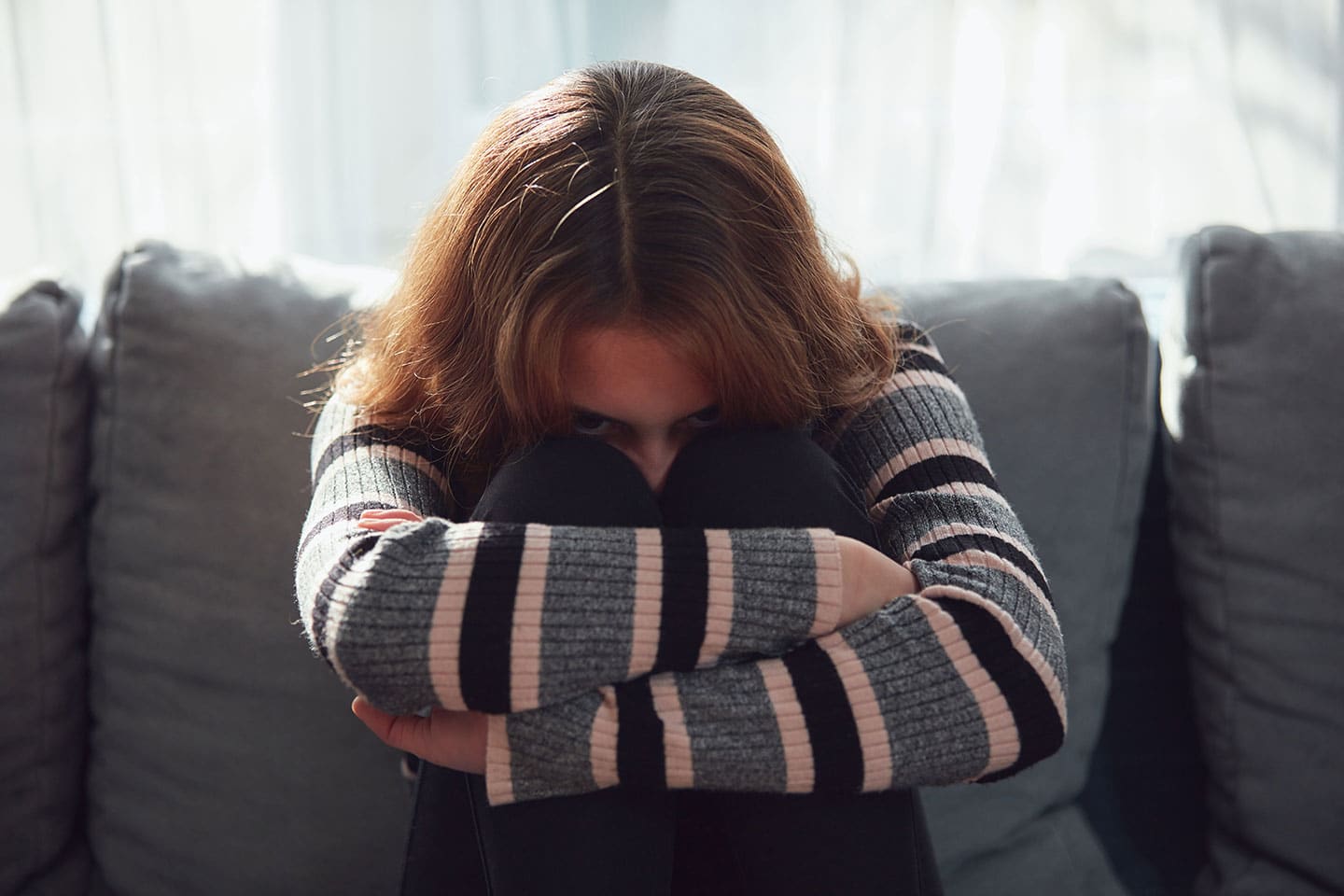 Ung kvinde sidder krøbet sammen på en sofa med armene om knæene, et udtryk for angst og overbelastning ved autisme